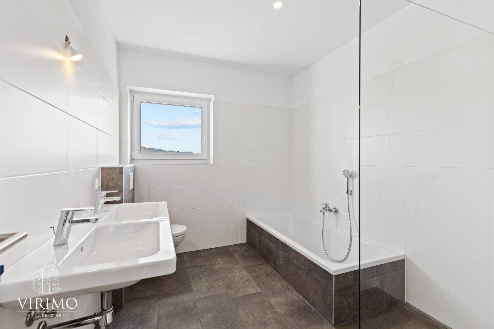 Modernes Badezimmer mit weißen Fliesen, Doppelwaschbecken, Badewanne und Fenster für Tageslicht.
