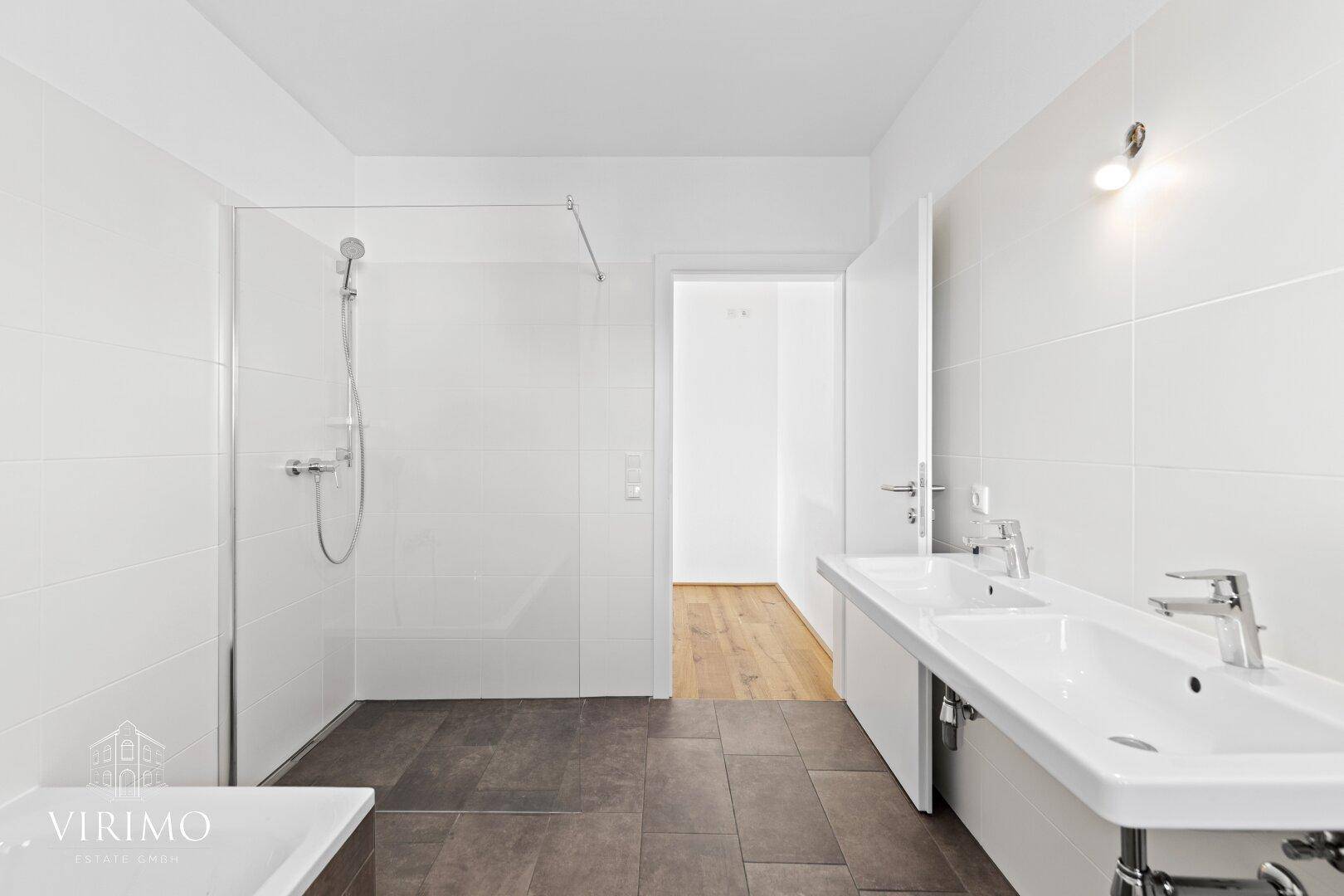 Helles Badezimmer mit Doppelwaschbecken, großer begehbarer Dusche und modernen Fliesen.