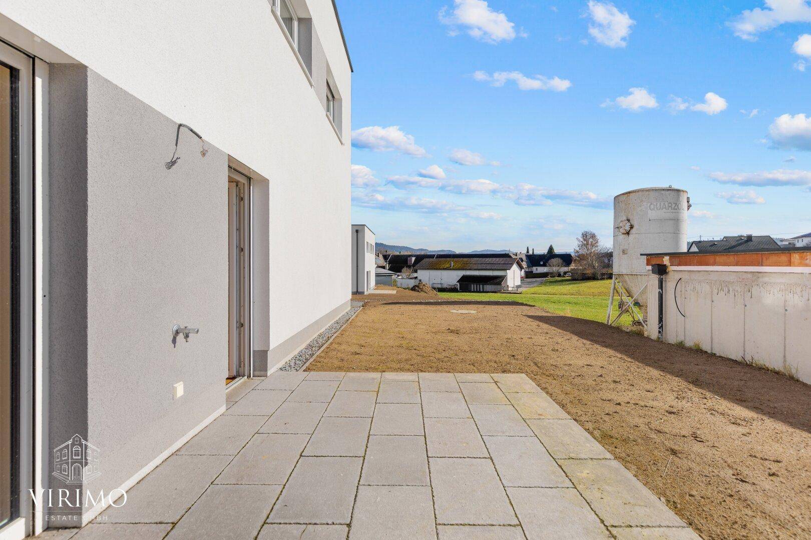 Gepflasterte Terrasse mit Zugang zu einem zukünftigen Gartenbereich, ideal für Entspannung im Freien.