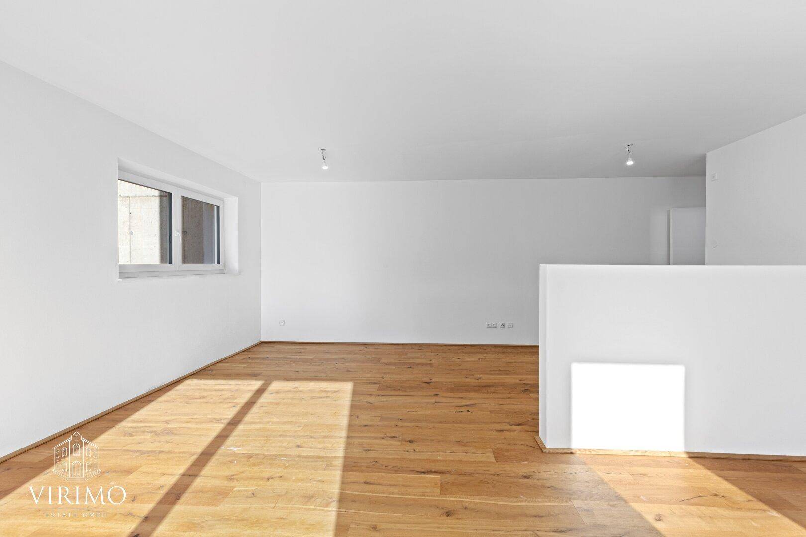 Geräumiger, heller Innenraum mit Holzboden und einem Fenster, das viel Tageslicht hereinlässt.
