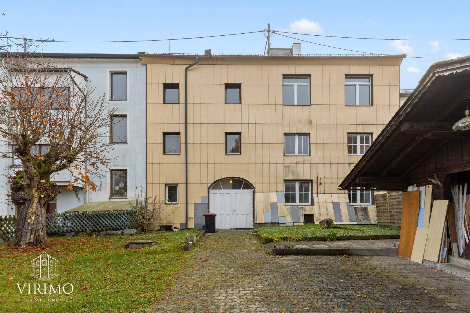Rückseite des Gebäudes mit gelber Fassade, Fenstern und einem Hinterhof mit Schuppen.