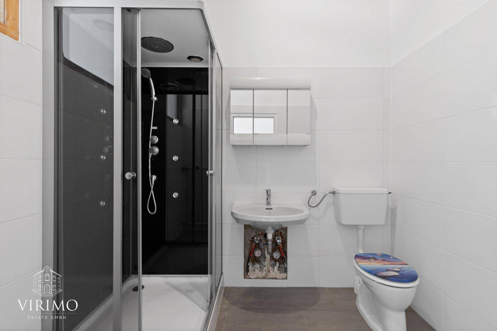 Badezimmer mit Duschkabine, Waschbecken und WC, weißen Fliesen und Spiegelschrank.