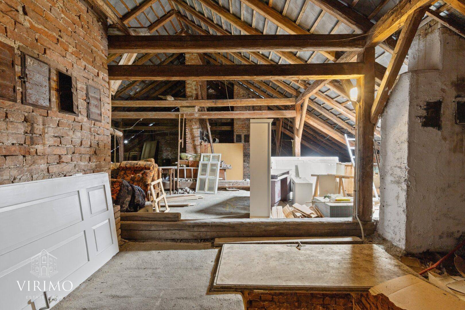 Unausgebauter Dachboden mit sichtbaren Holzbalken und Ziegelwänden, viel Stauraum.