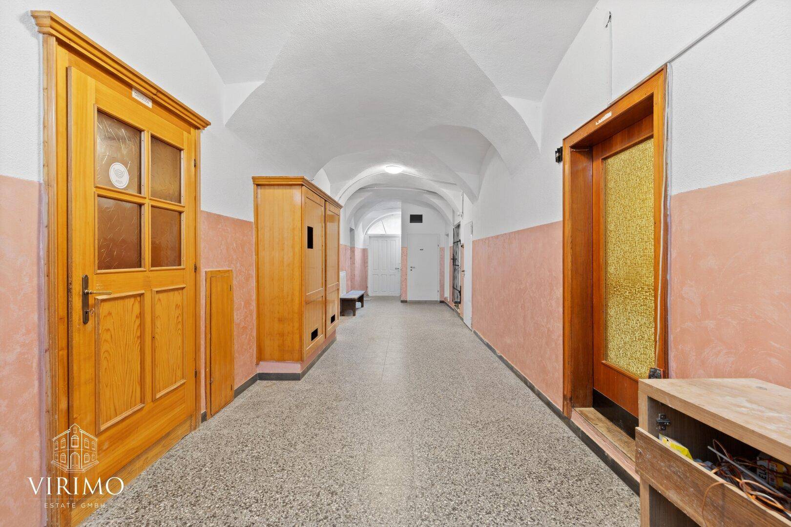 Langer Flur mit Terrazzoboden, gewölbter Decke und Holztüren in einem historischen Gebäude.