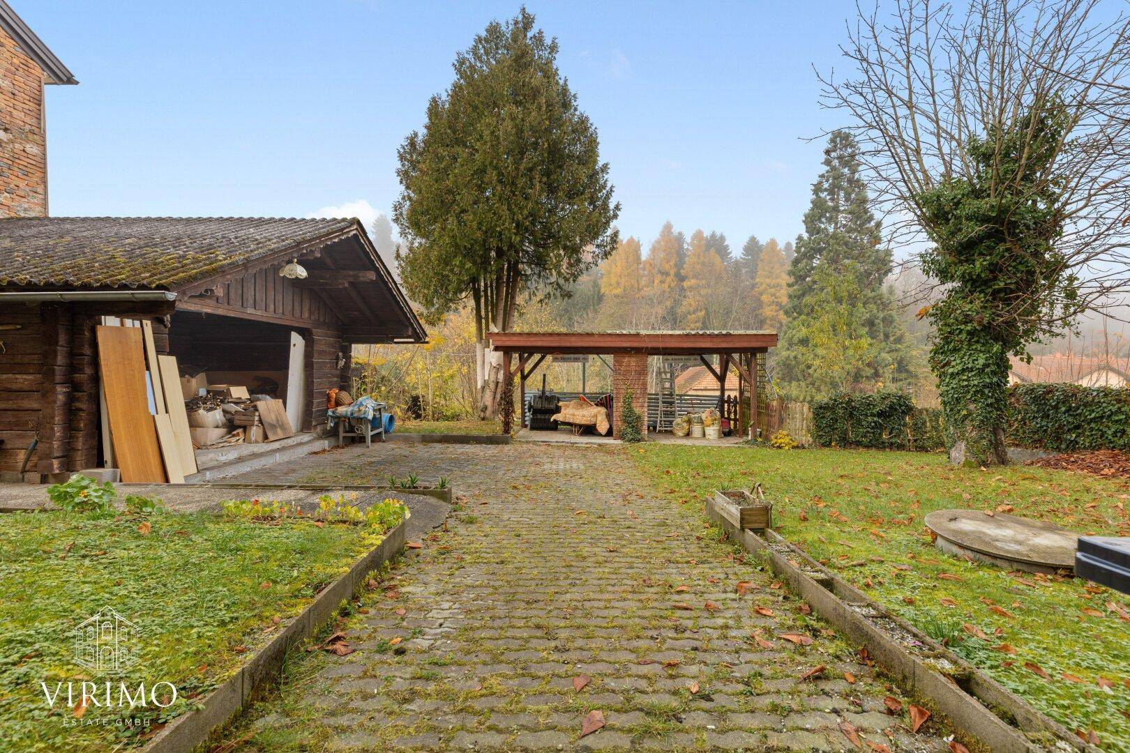 Großer Hinterhof mit gepflastertem Weg, Rasenfläche und Holzschuppen.