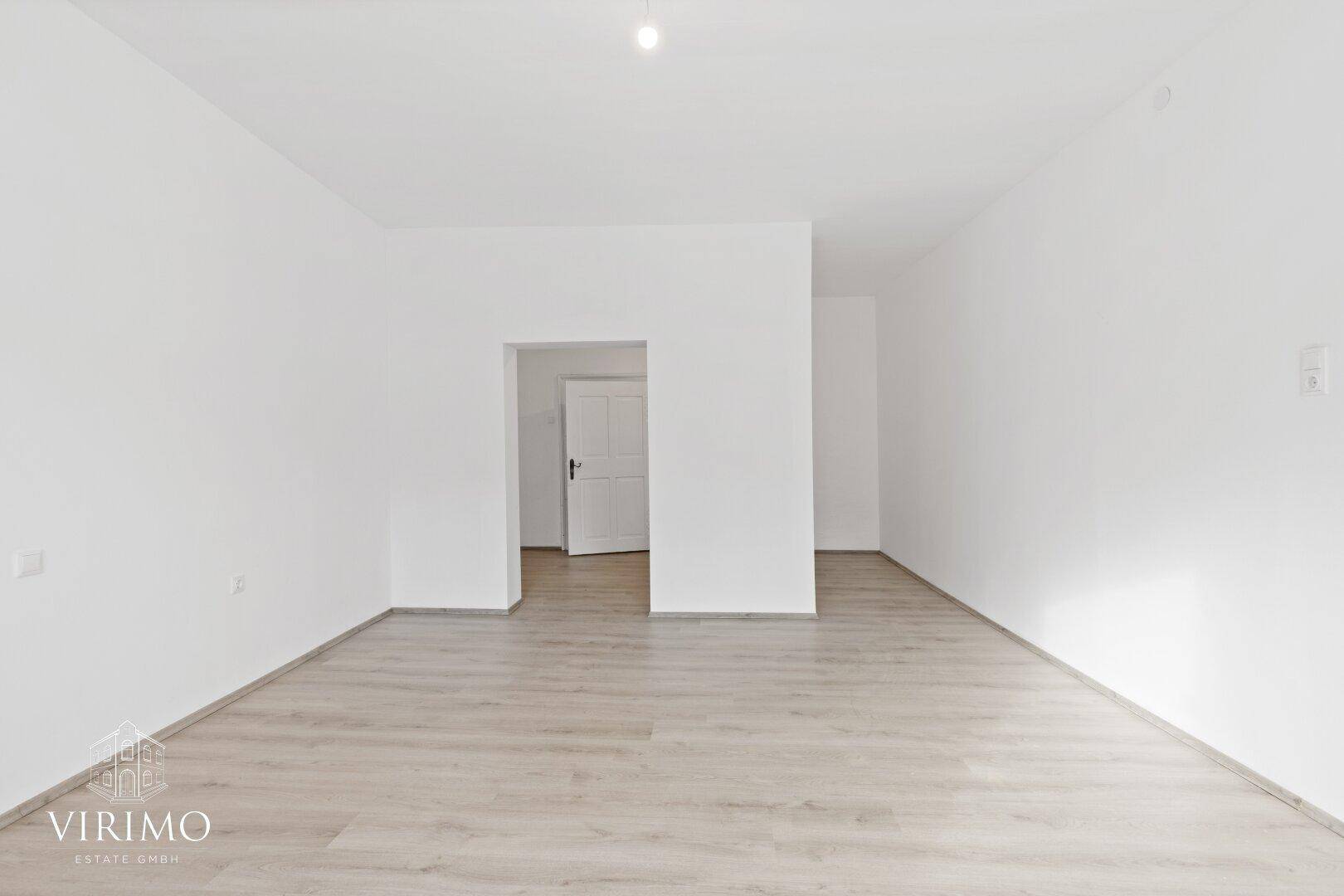 Leerer Raum mit hellem Laminatboden und einem Durchgang zu weiteren Zimmern.