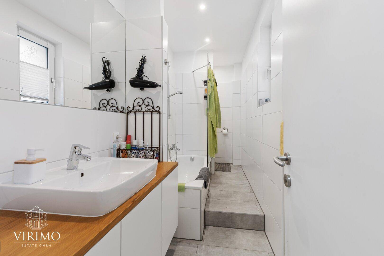 Helles Badezimmer mit Badewanne, modernem Waschtisch und einem Fenster für Tageslicht.