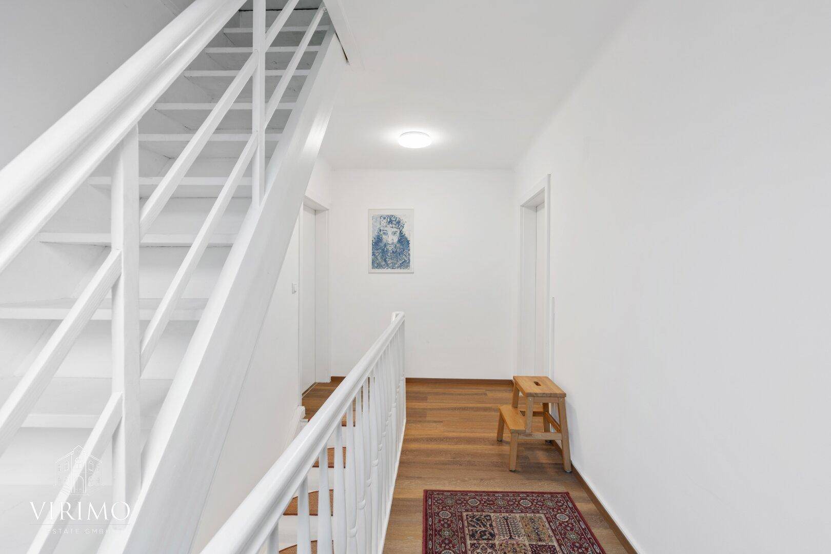 Heller Treppenaufgang mit weißem Geländer und Holzboden im Obergeschoss des Hauses.