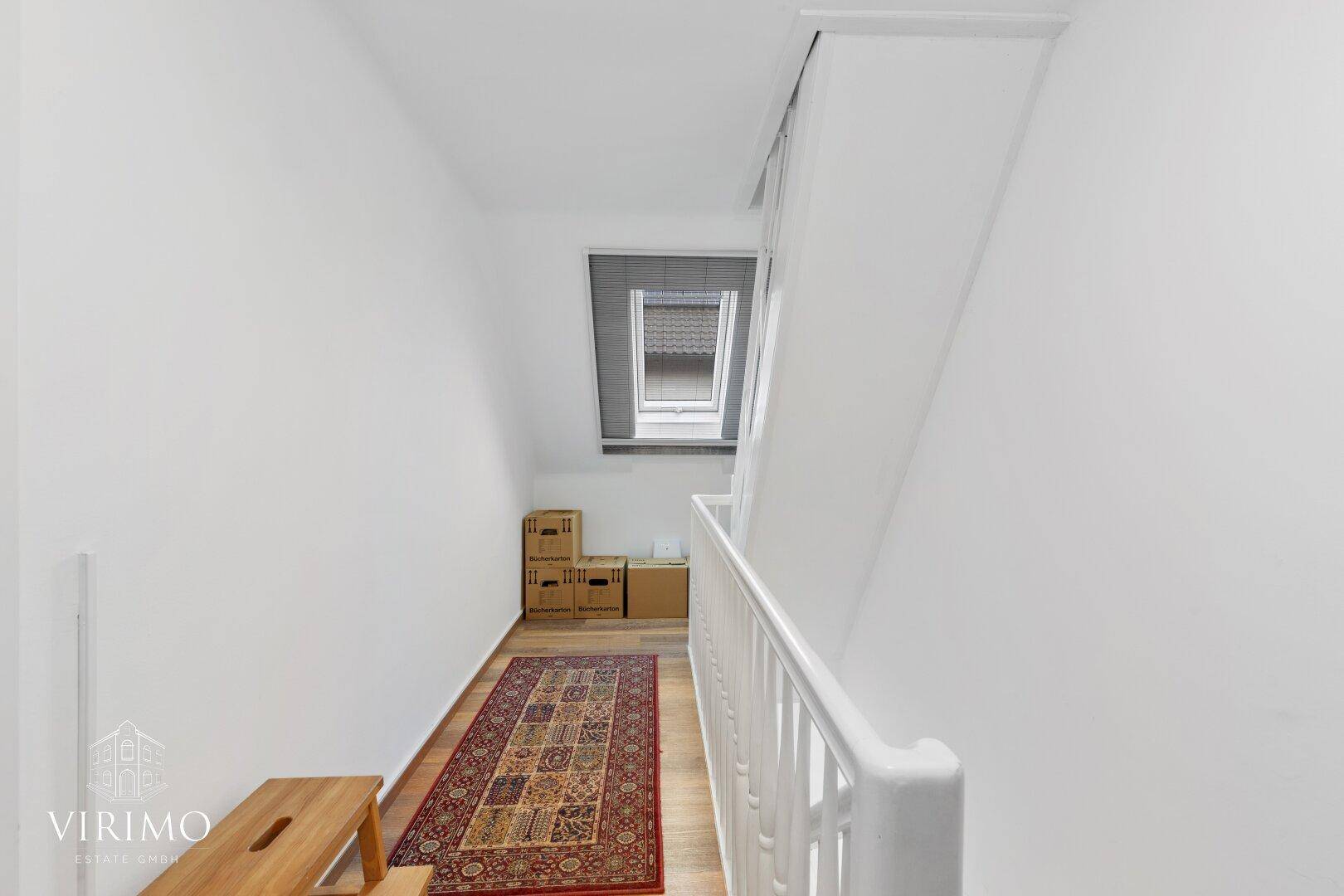 Dachgeschossflur mit Dachfenster, Holzboden und praktischem Stauraum für Kartons.