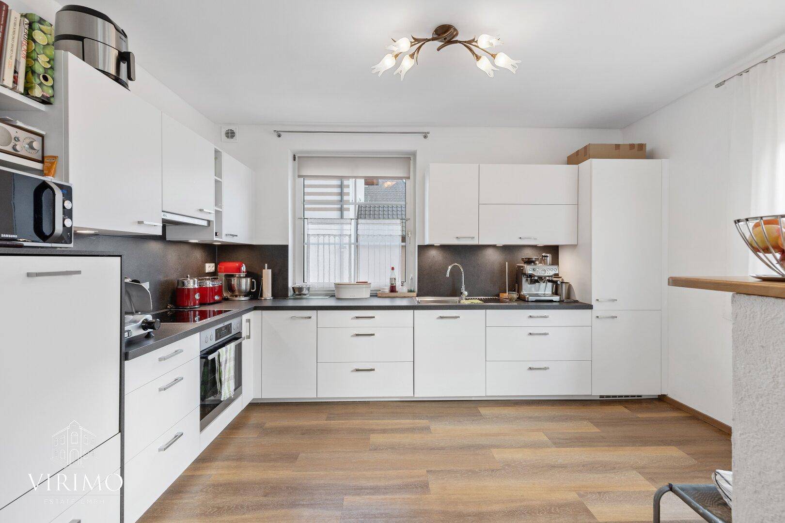 Moderne weiße Einbauküche mit dunkler Arbeitsplatte, Induktionskochfeld und Fenster.