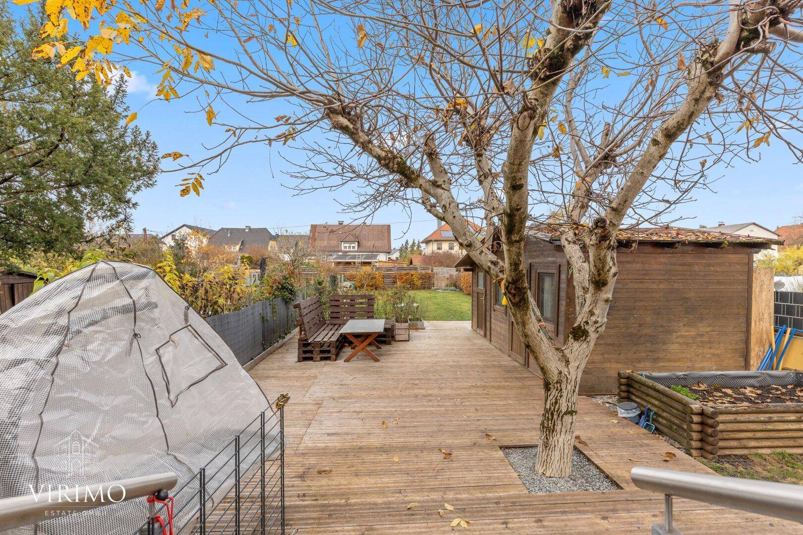 Weitläufige Holzterrasse im Garten mit Sitzbank und Blick auf die Umgebung.