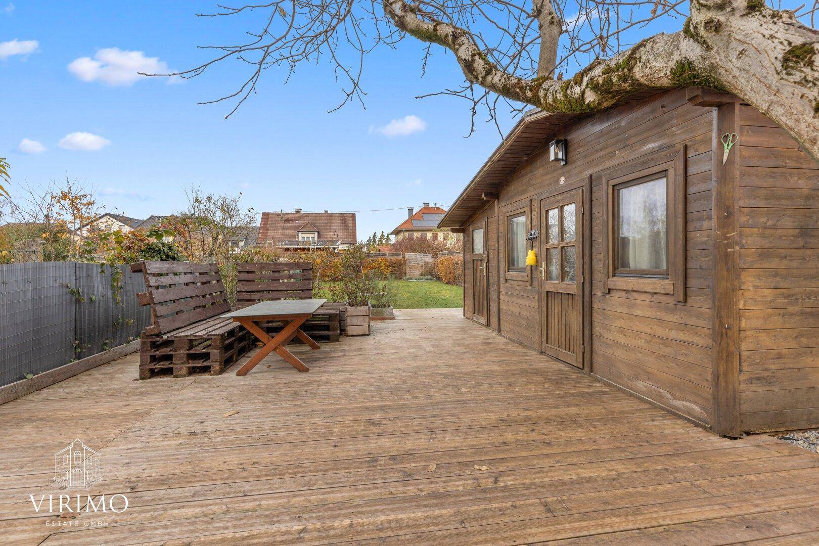 Geräumige Holzterrasse mit Gartenhaus und rustikaler Sitzgruppe im Freien.