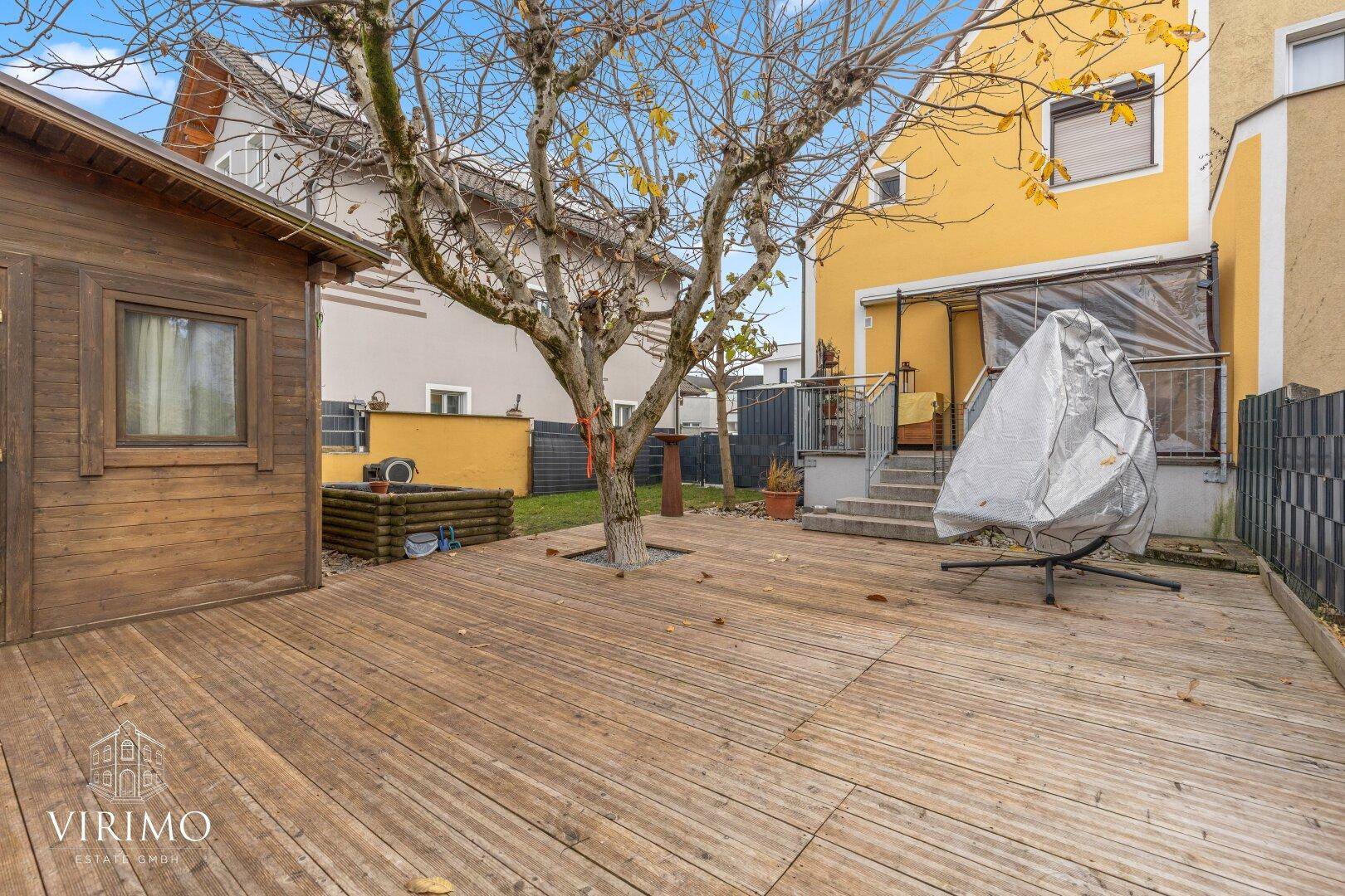 Große Holzterrasse im Garten mit einem Baum und einem charmanten Gartenhaus.