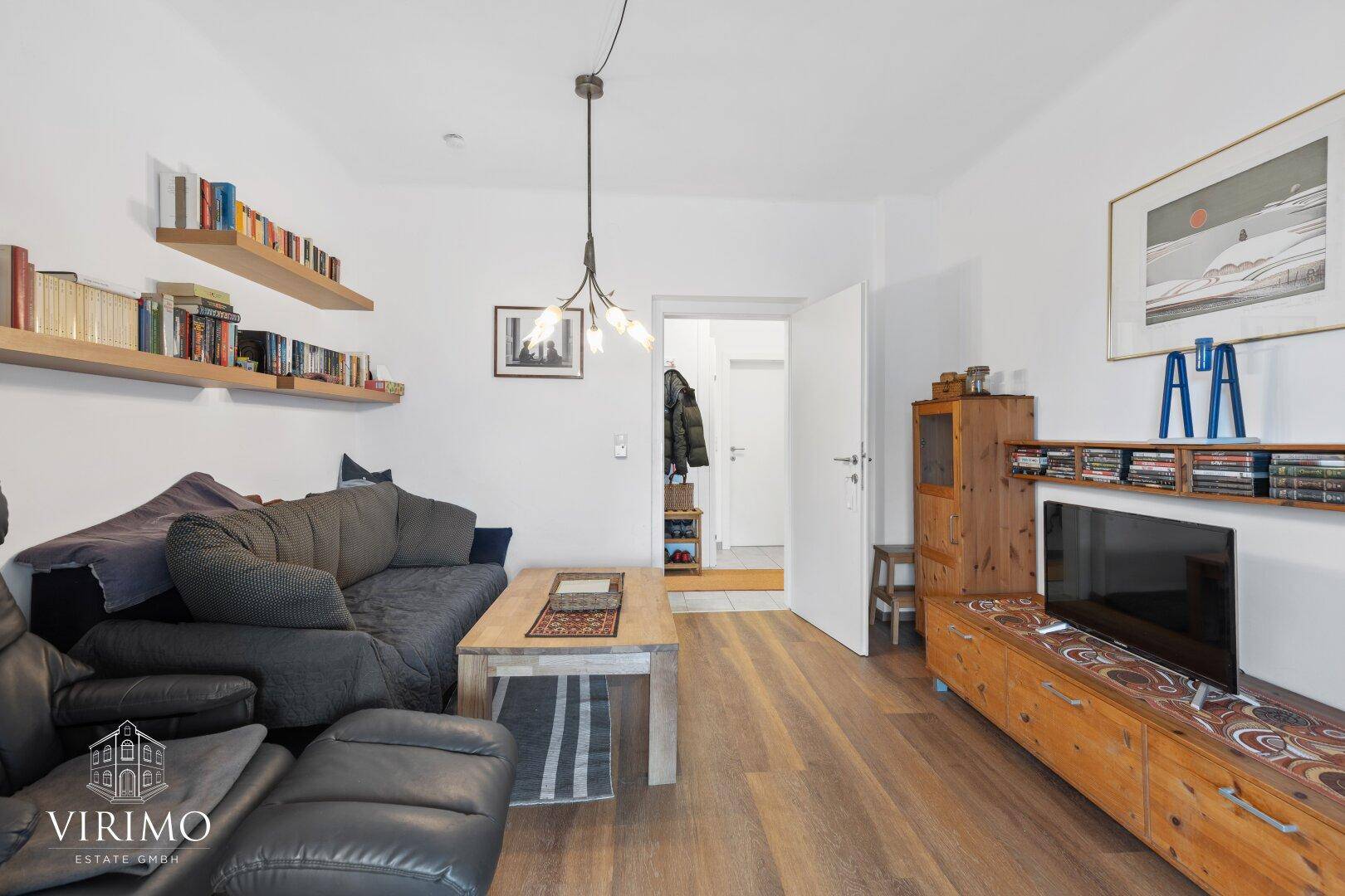 Heller Wohnbereich mit Sofa, TV-Möbel und Blick in den angrenzenden Flur.