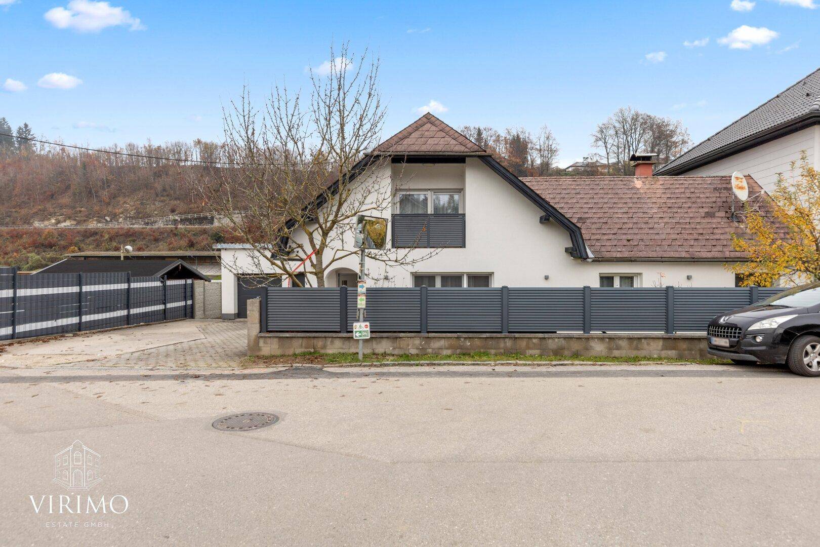 Ansicht des Einfamilienhauses von der Straße mit Zaun und gepflasterter Zufahrt.