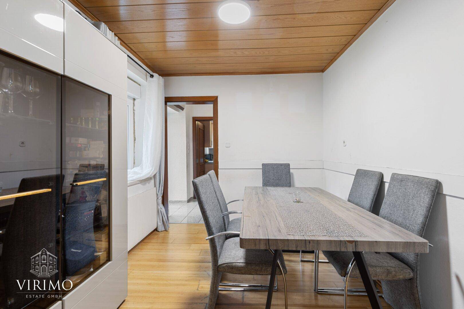 Esszimmer mit Holztisch, grauen Stühlen und Holzpaneeldecke.