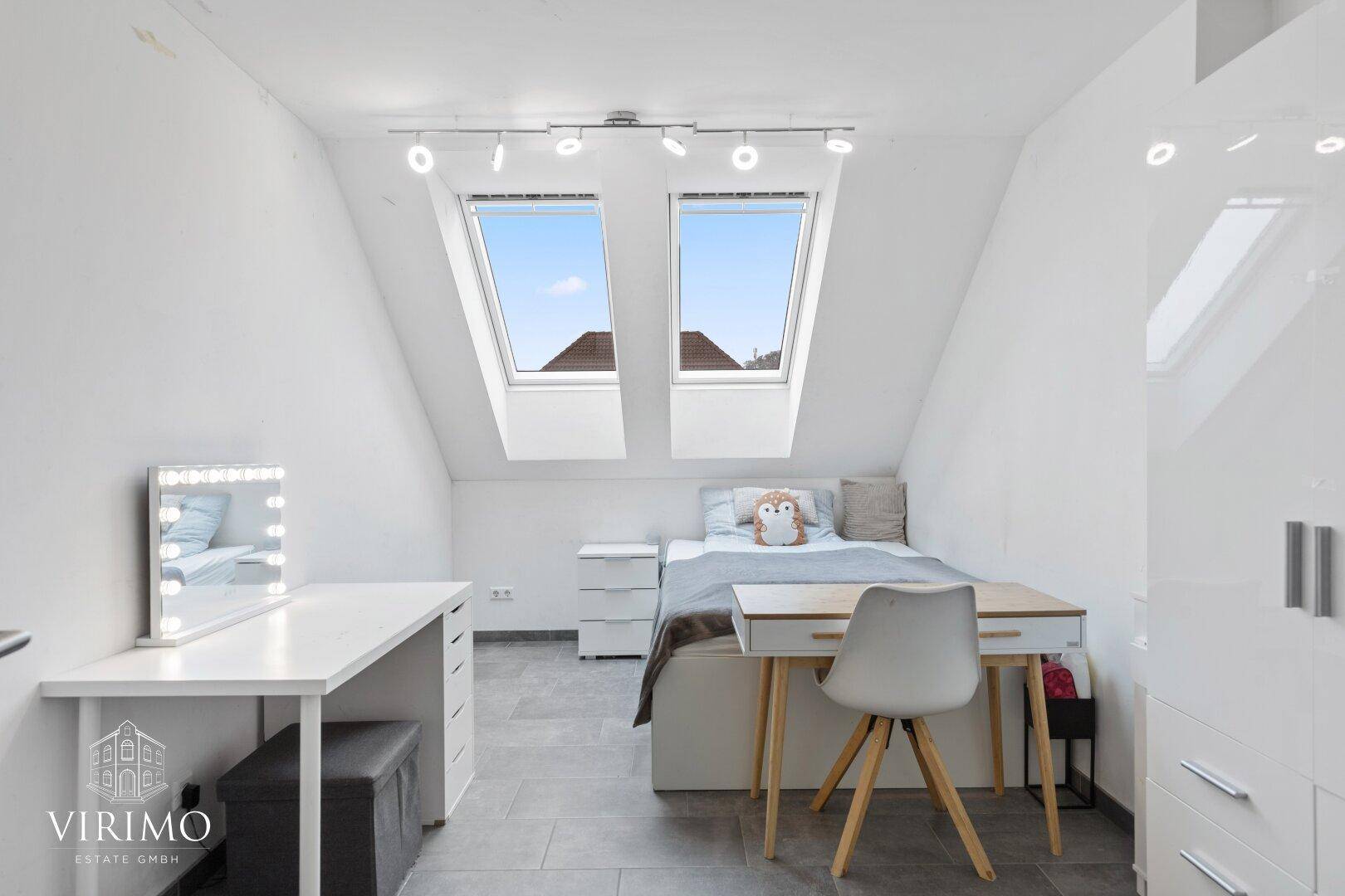 Helles Dachgeschoss-Schlafzimmer mit zwei Dachfenstern, Schreibtisch und modernem Dekor.