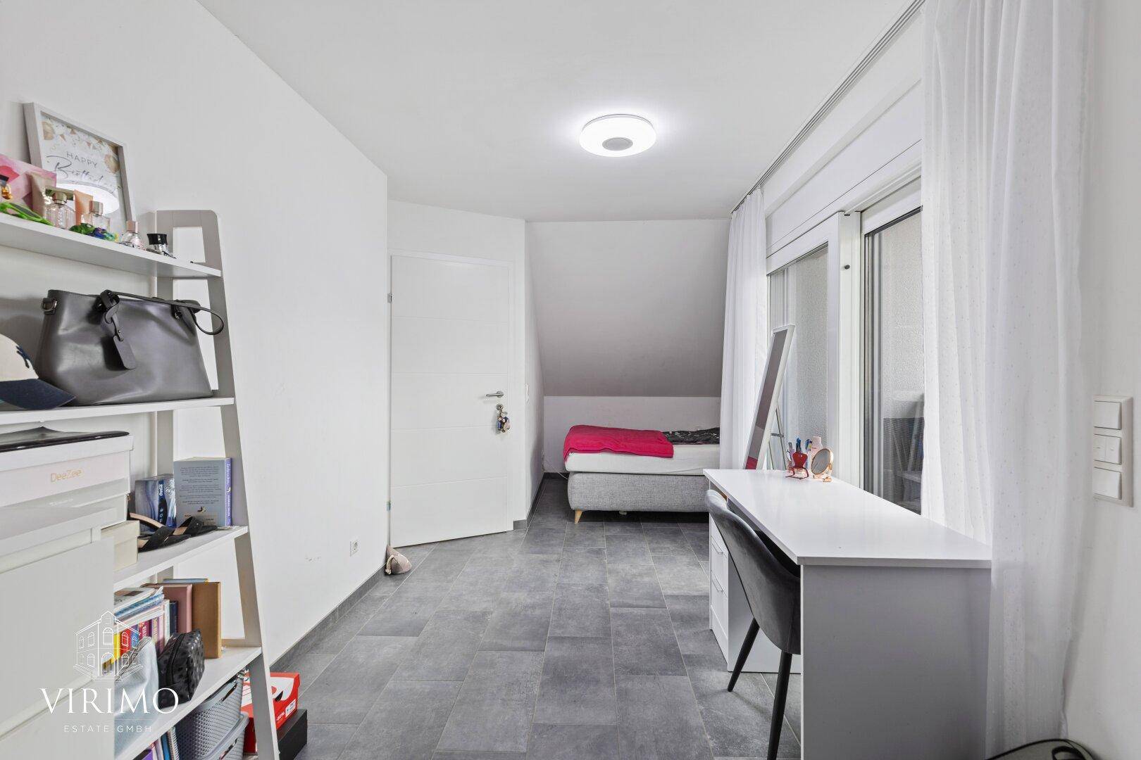 Dachgeschosszimmer mit Schreibtisch, Regal und Zugang zu einem kleinen Balkon.