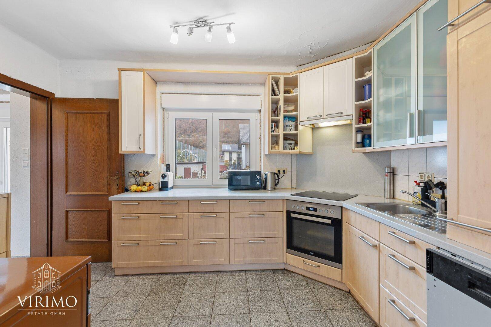 Einbauküche mit hellen Holzfronten, Fliesenboden und Fenster mit Ausblick.