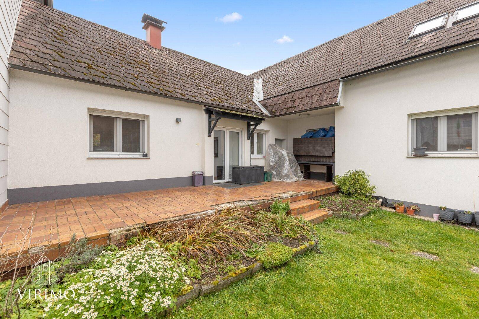 Hinterhof mit gepflasterter Terrasse, Rasenfläche und Zugang zum Haus.