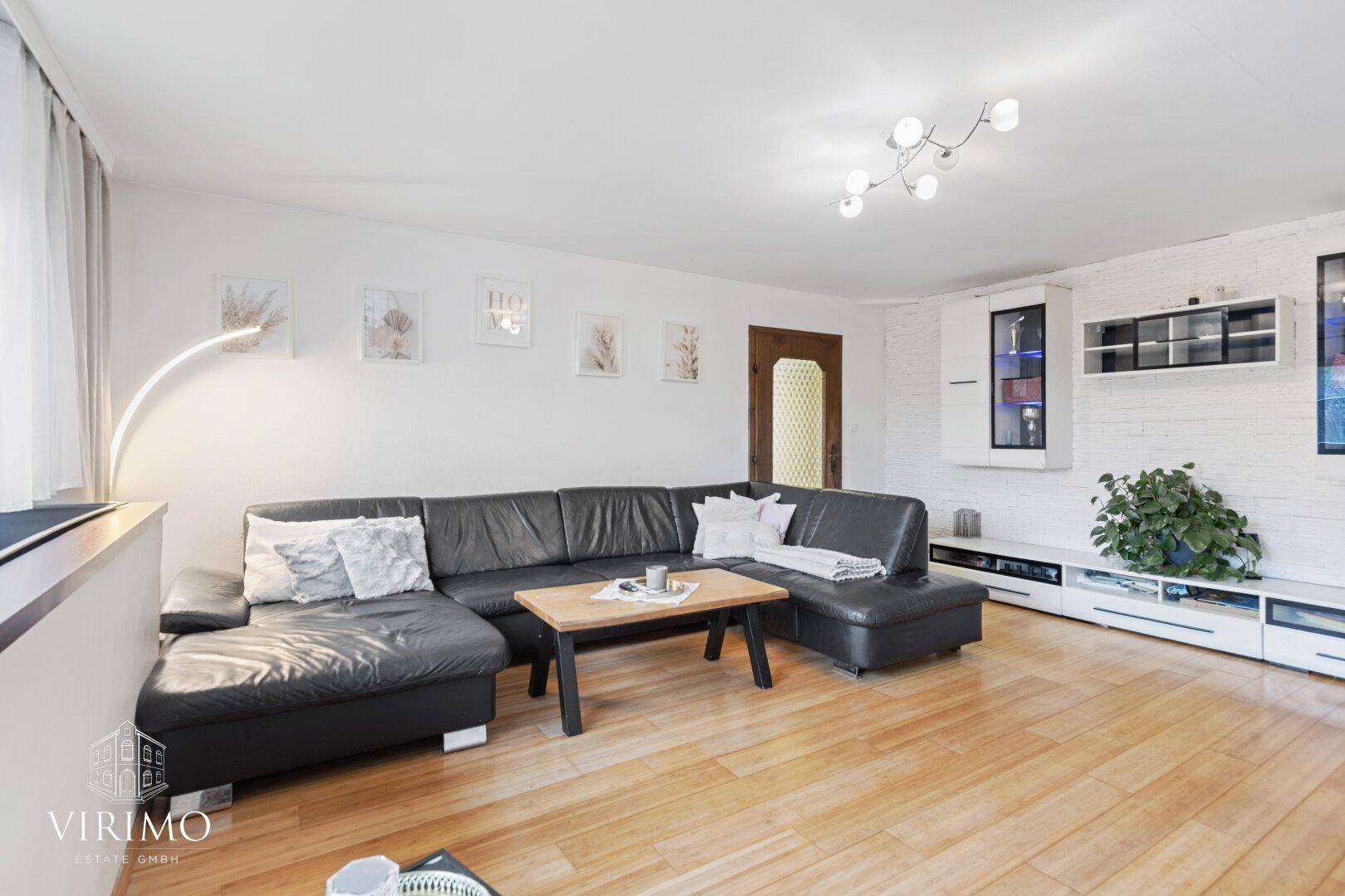Gemütliches Wohnzimmer mit großem Ecksofa, Holzboden und moderner Deckenleuchte.