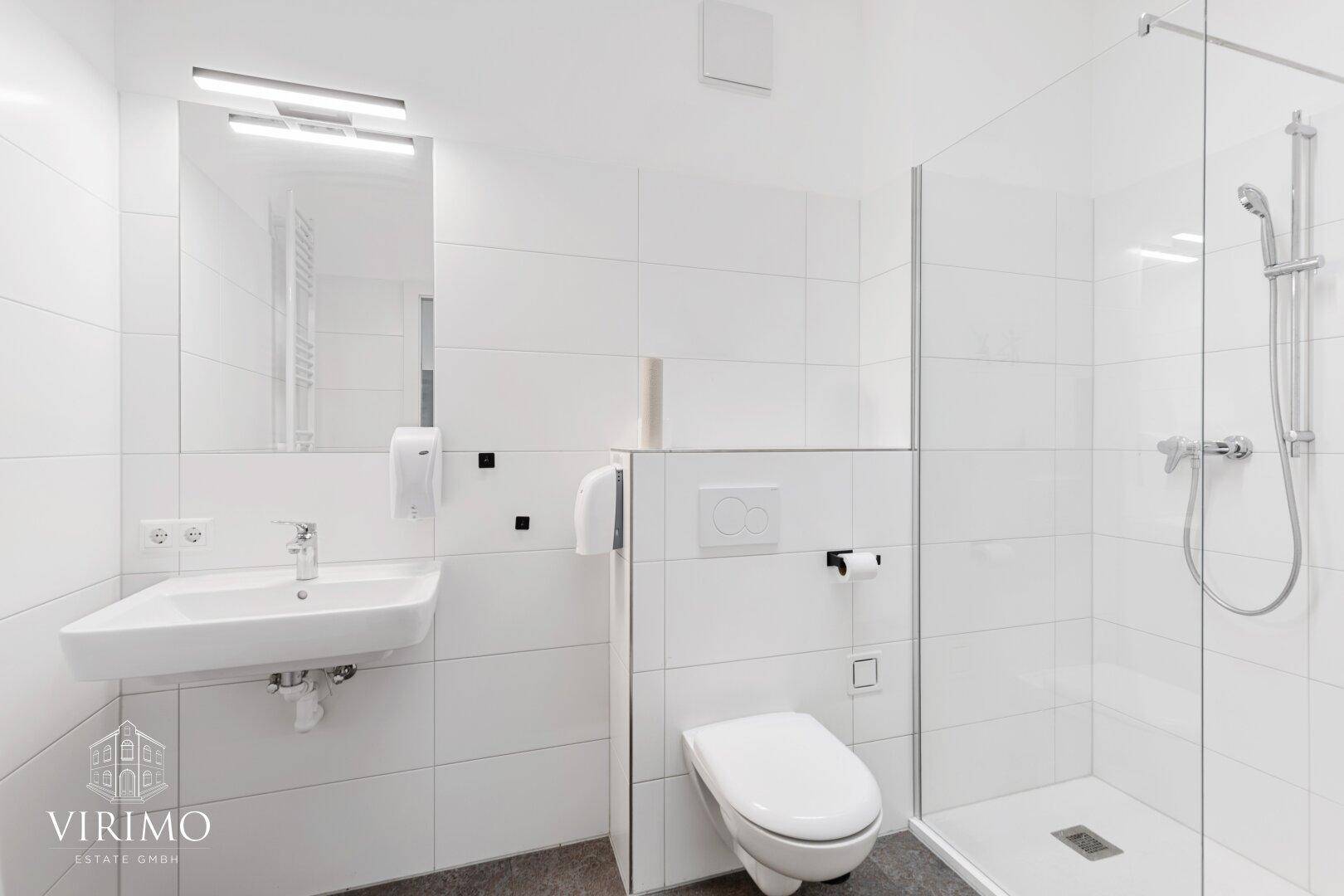 Sauberes Badezimmer mit modernem Waschbecken, Toilette und großformatigen weißen Fliesen.