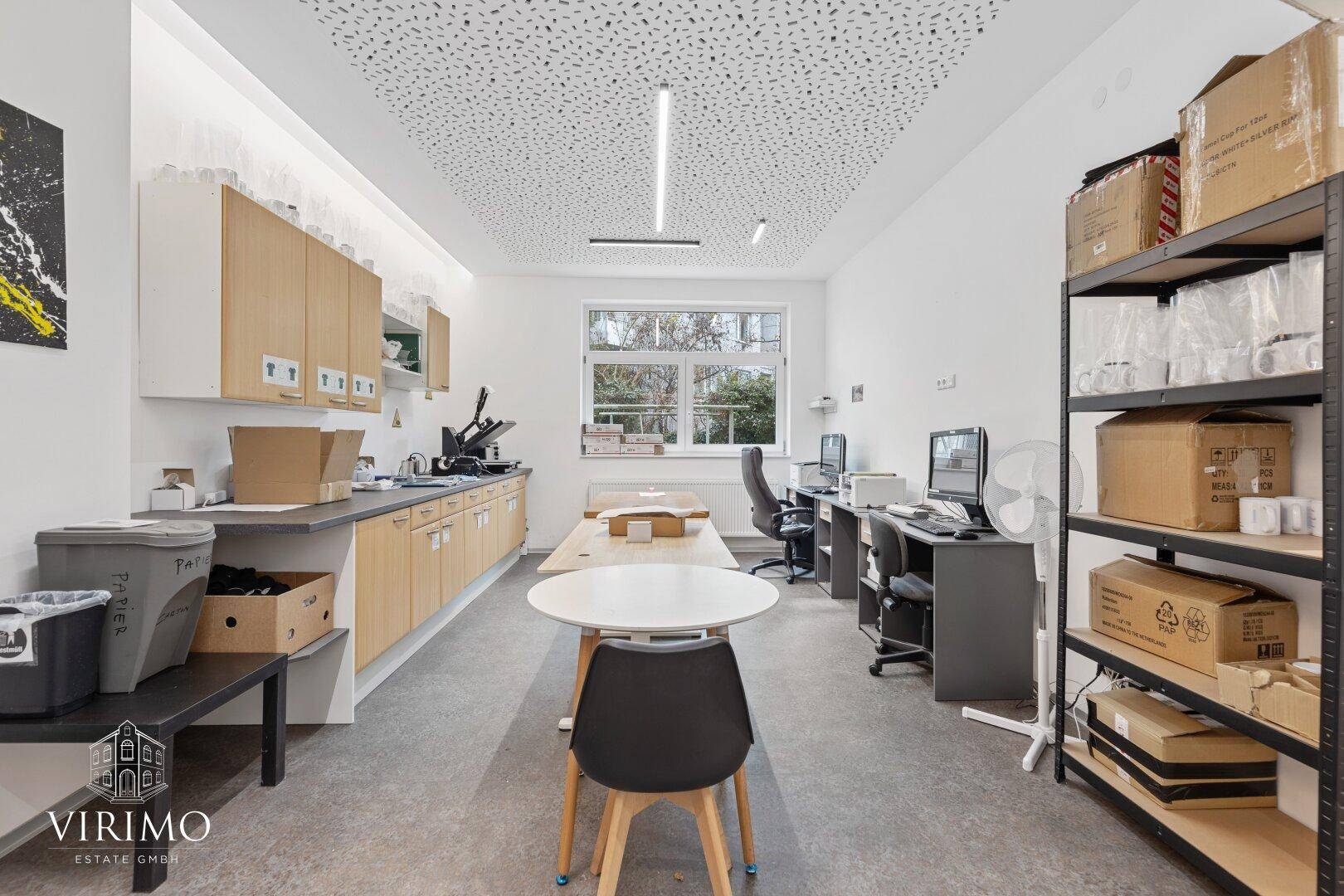 Geräumiger Arbeitsbereich mit mehreren Tischen, Regalen und einer langen Arbeitsplatte entlang der Wand.