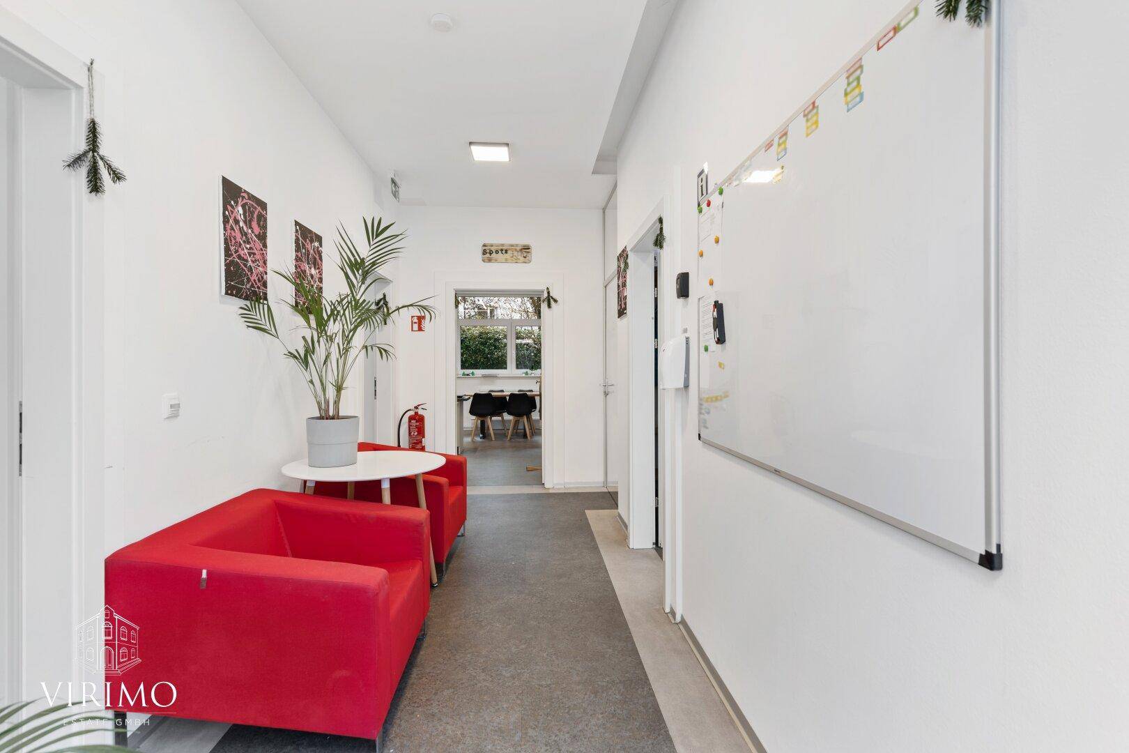 Heller Flur mit rotem Sofa, Zimmerpflanze und einem Whiteboard an der Wand.