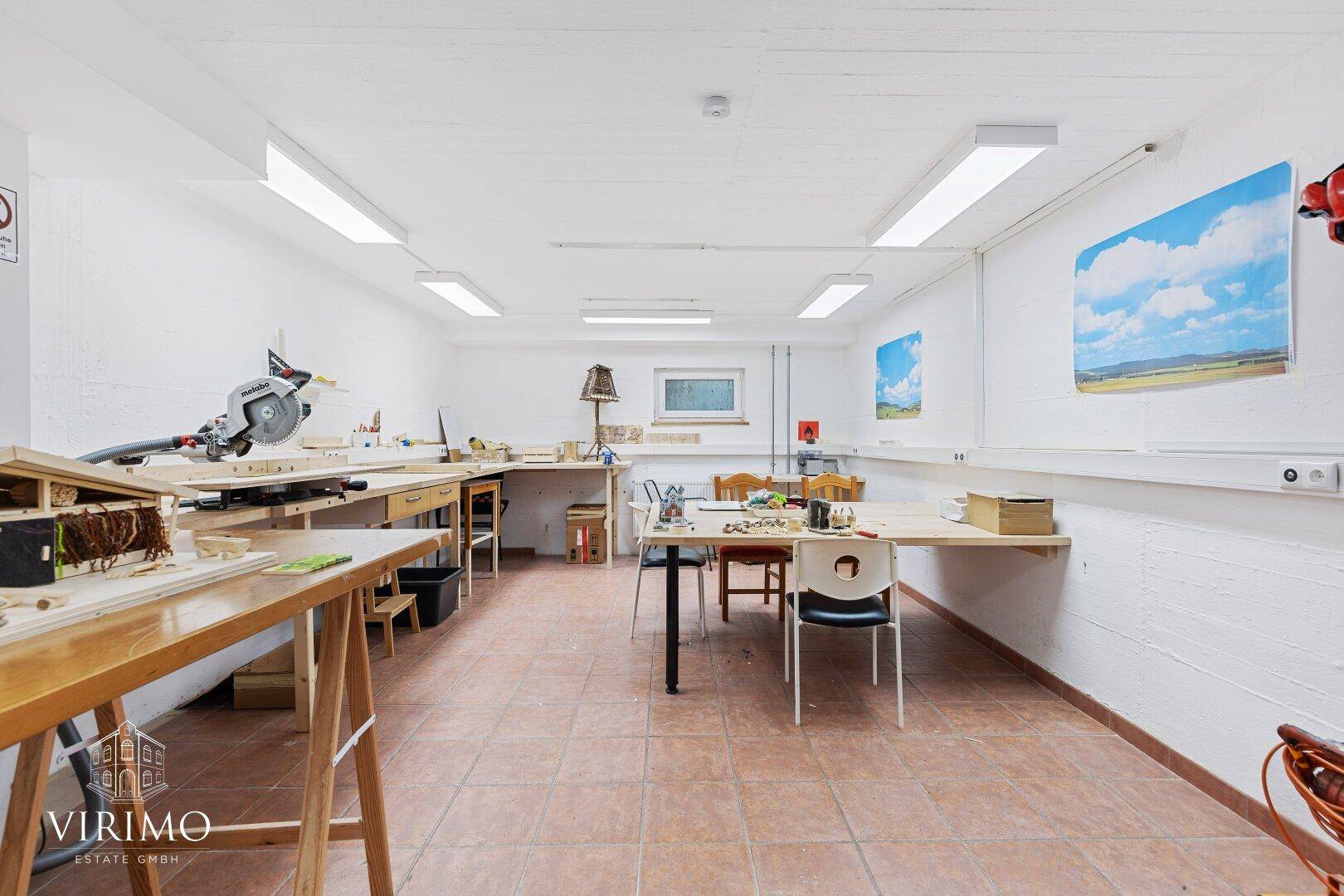 Geräumiger Werkstattraum im Untergeschoss mit Arbeitsflächen, Werkzeugen und Fliesenboden.
