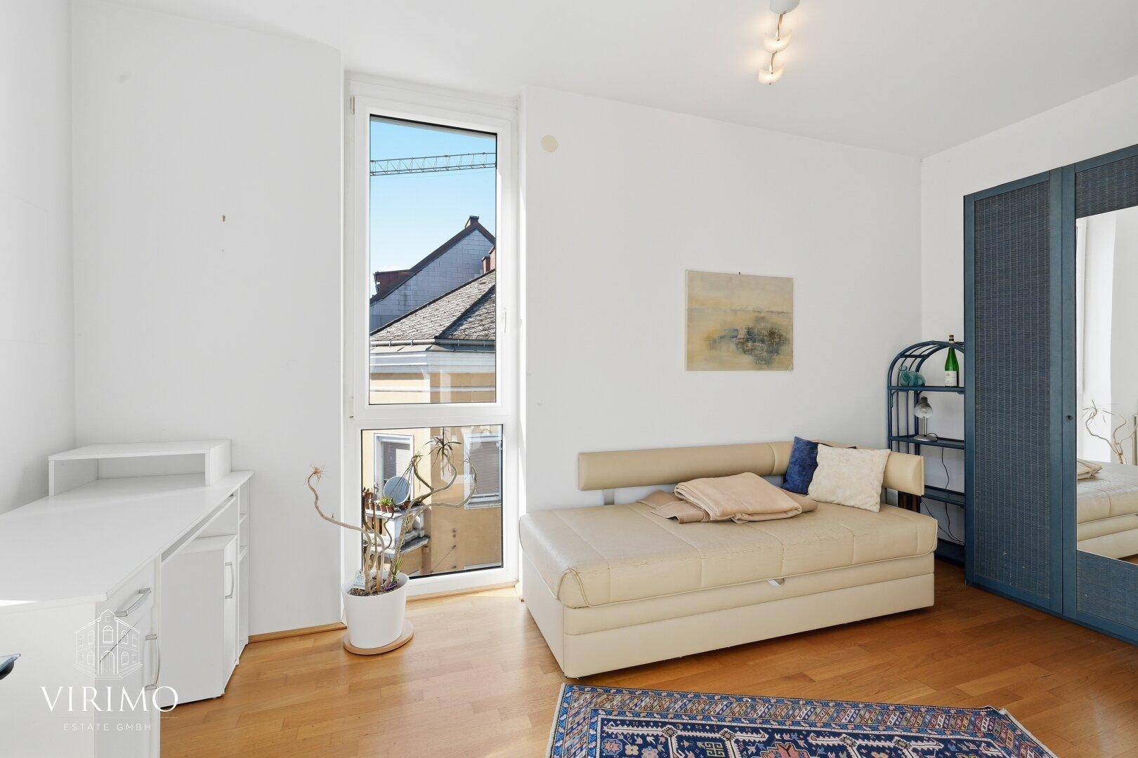 Arbeitszimmer mit Tagesbett, Kleiderschrank und hohen Fenstern, die viel Tageslicht hereinlassen.