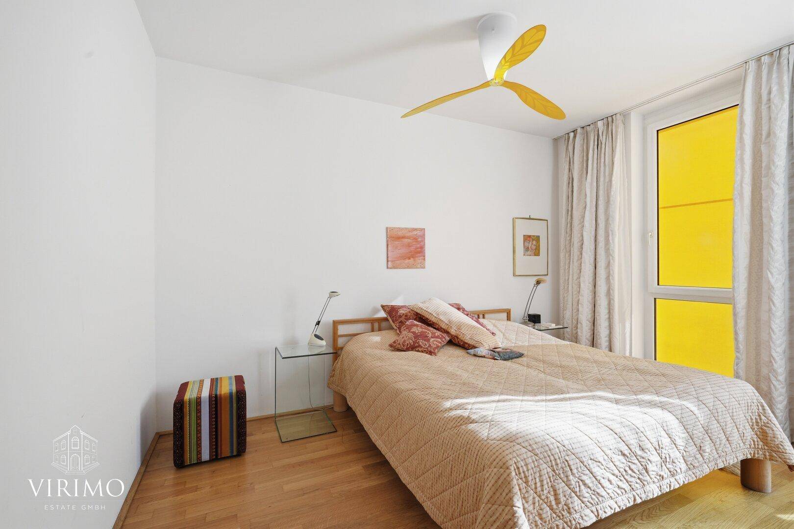 Helles Schlafzimmer mit Doppelbett, gelbem Deckenventilator und großem Fenster für viel Licht.