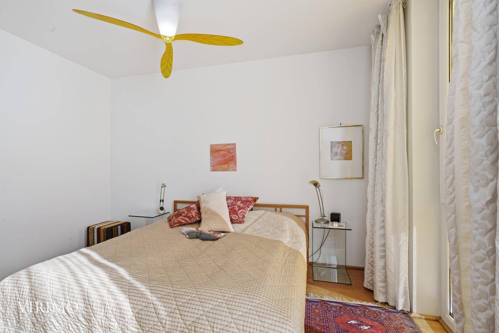 Schlafzimmer mit Holzboden, Teppich, Nachttischen und einem auffälligen Deckenventilator.