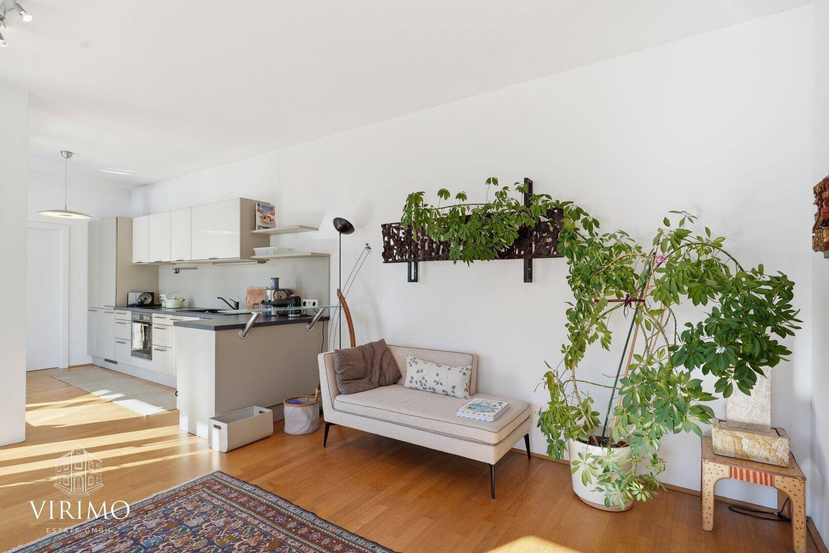Gemütlicher Wohnbereich mit Sofa, vielen Pflanzen und Blick auf die moderne Küchenzeile.