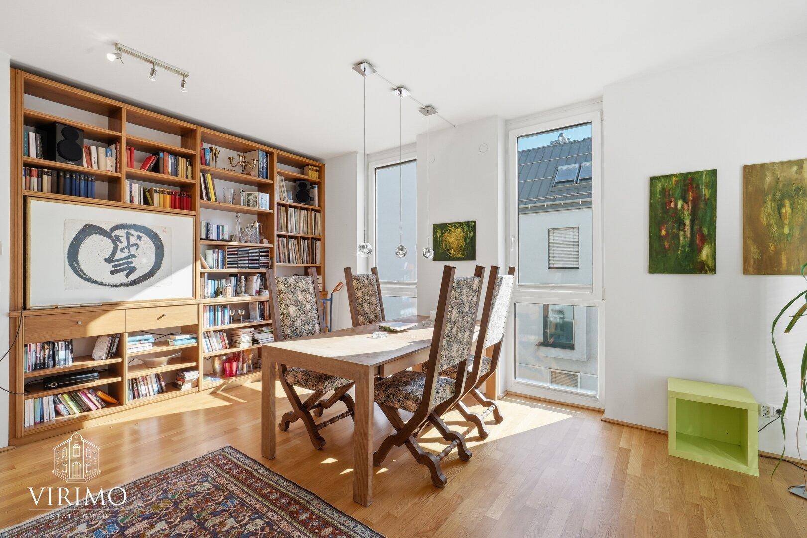 Essbereich mit großem Holzbücherregal, Esstisch und viel Tageslicht durch hohe Fenster.