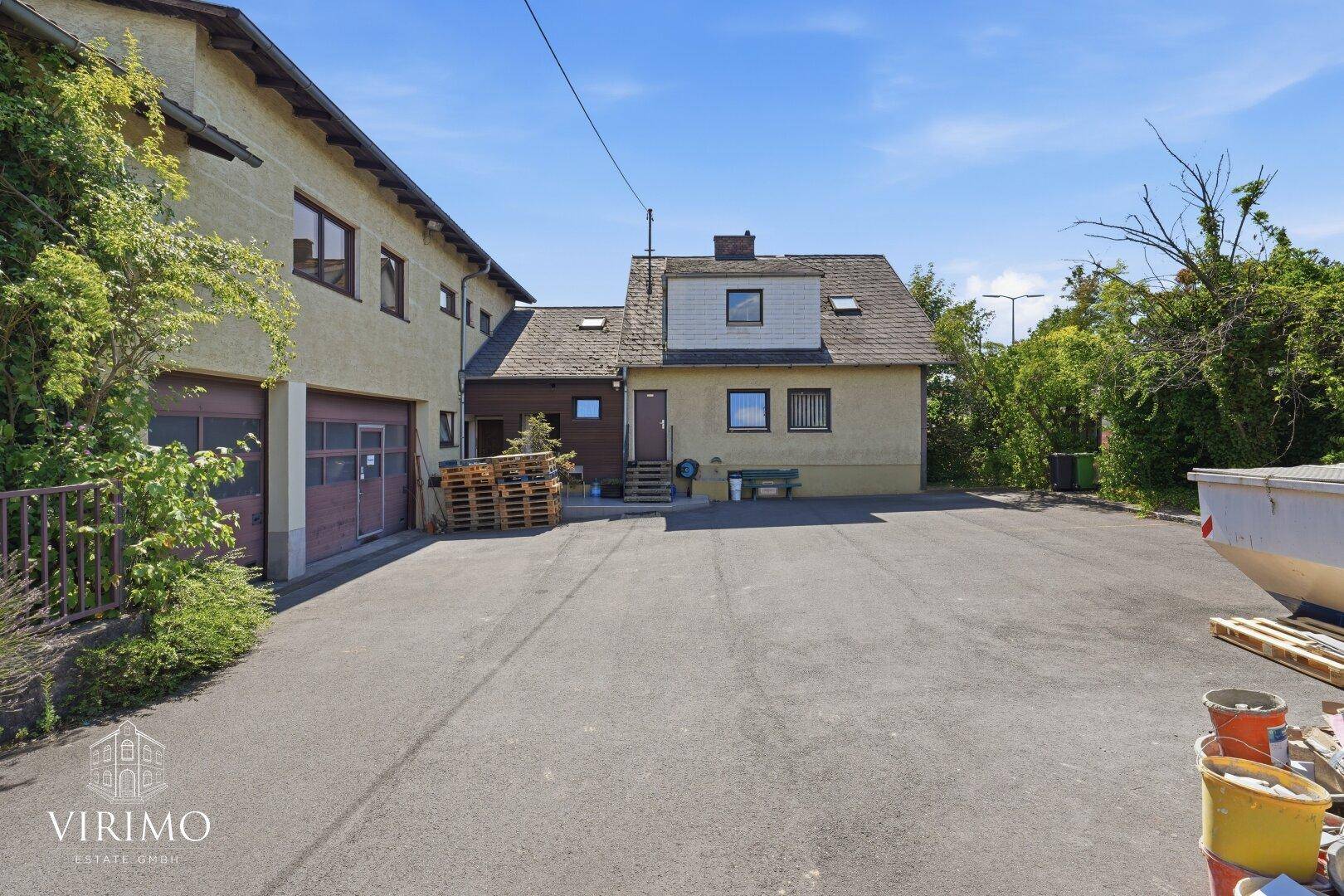 Außenansicht des Gebäudes mit Garagen und großem Vorplatz unter blauem Himmel.