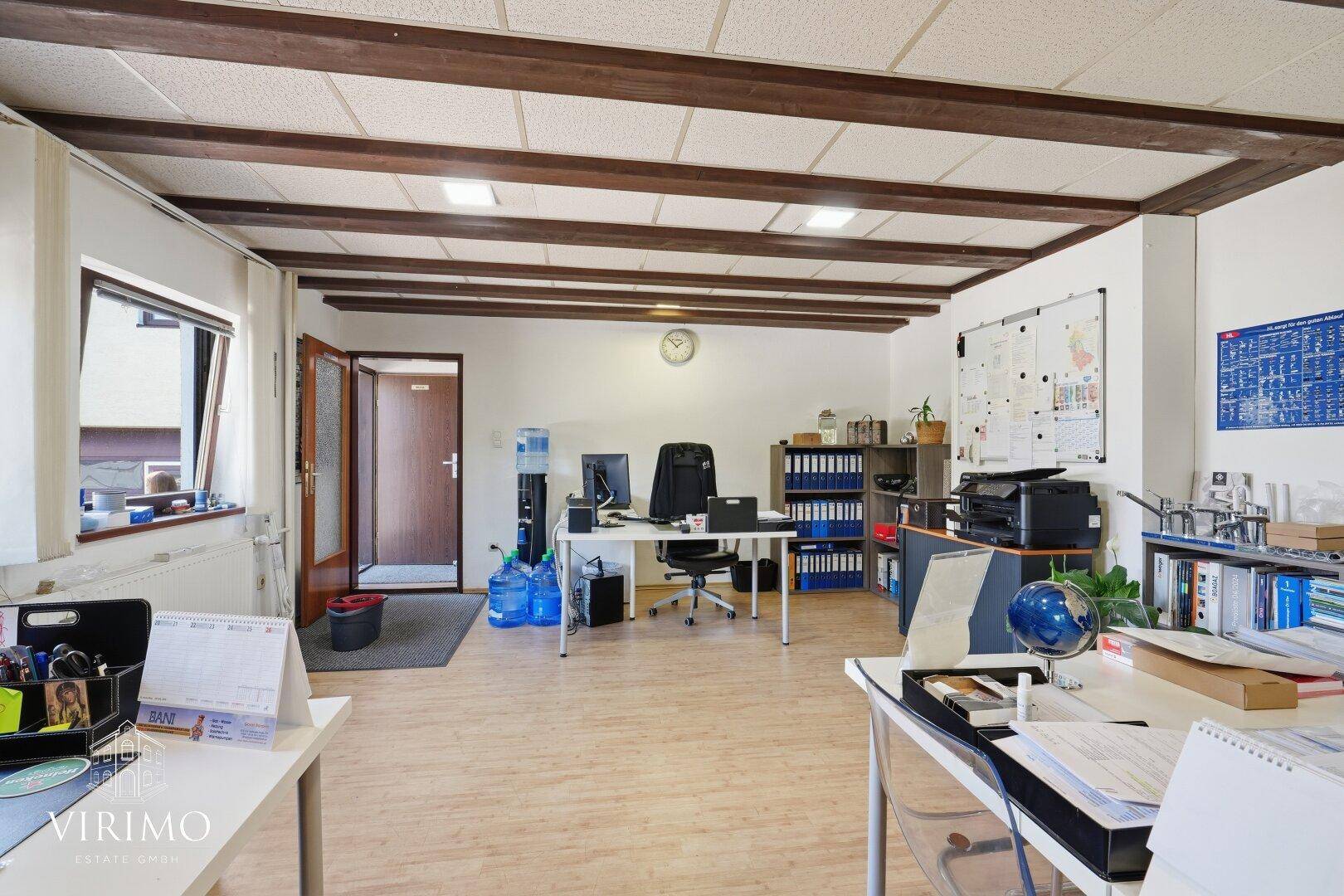 Großes Büro mit Holzbalkendecke, mehreren Arbeitsplätzen und Fenstern.