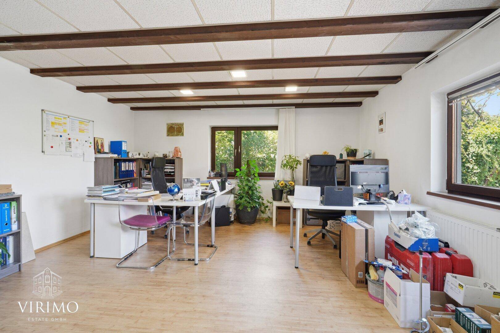 Helles Büro mit Holzbalkendecke, Schreibtischen und Blick ins Grüne.
