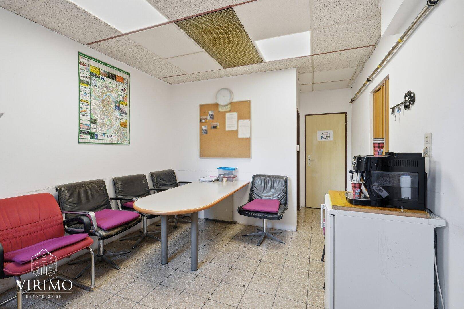 Wartebereich oder kleines Büro mit Sitzgelegenheiten, Tisch und Kaffeemaschine.