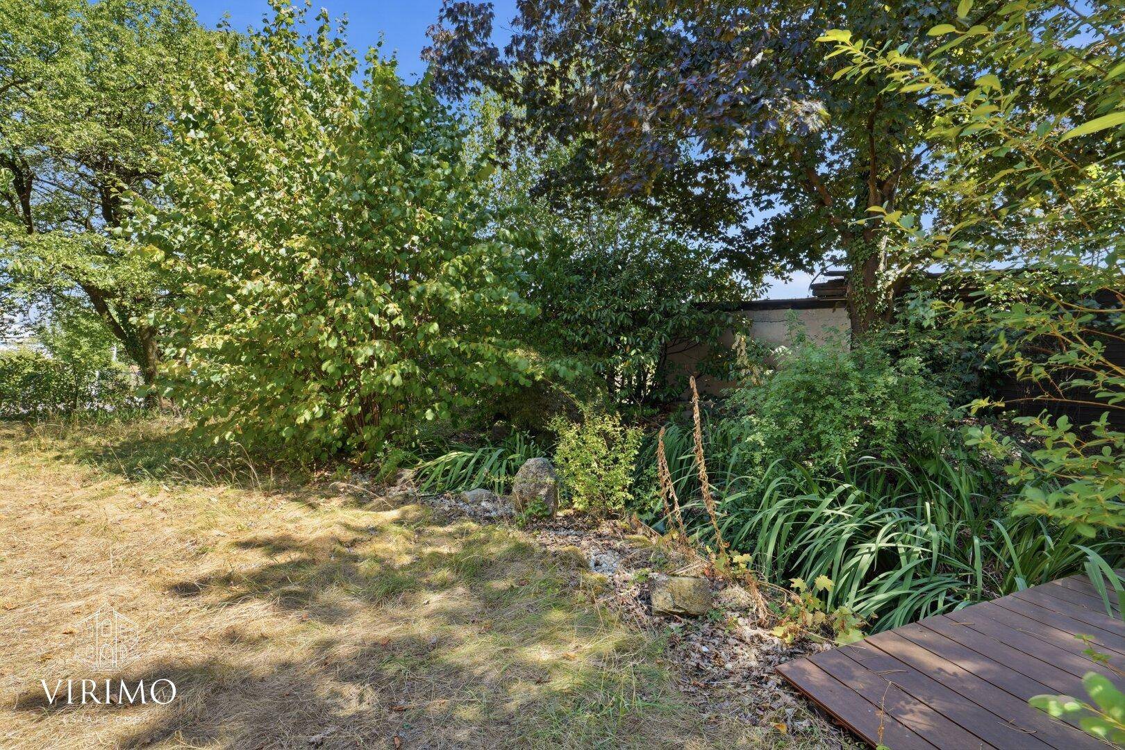 Naturbelassener Gartenbereich mit Bäumen, Sträuchern und Holzdeck.