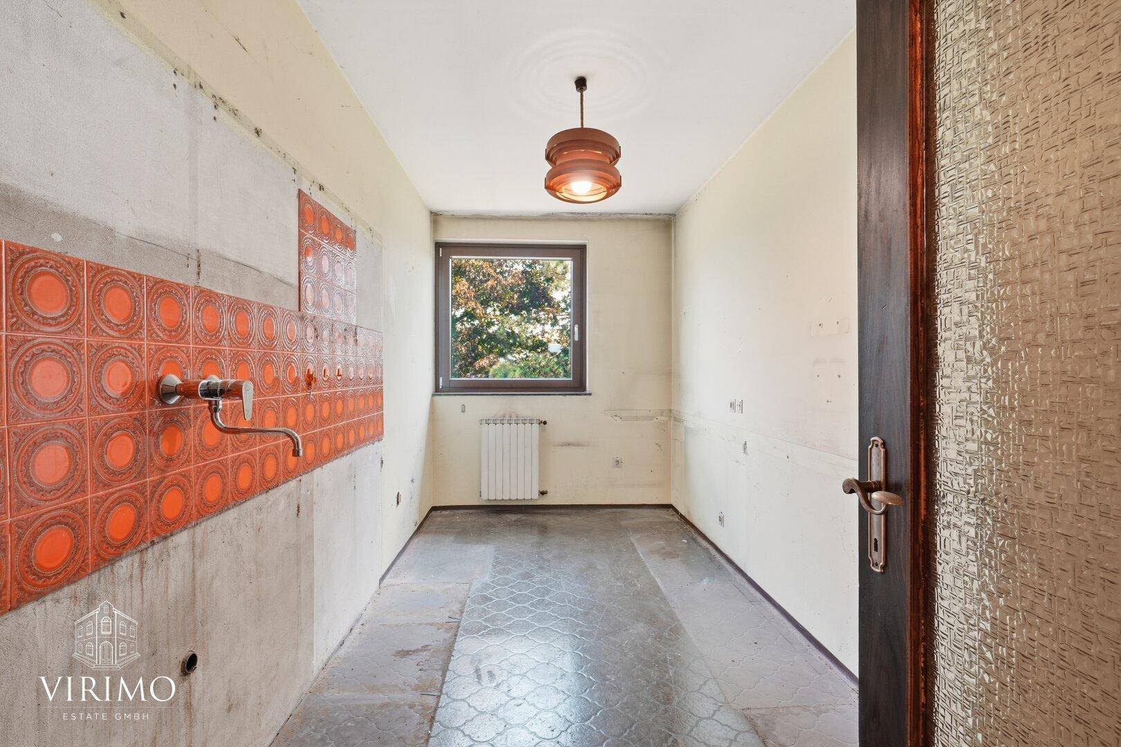 Küche mit orangefarbenen Fliesen und Fenster, bereit für eine Modernisierung.