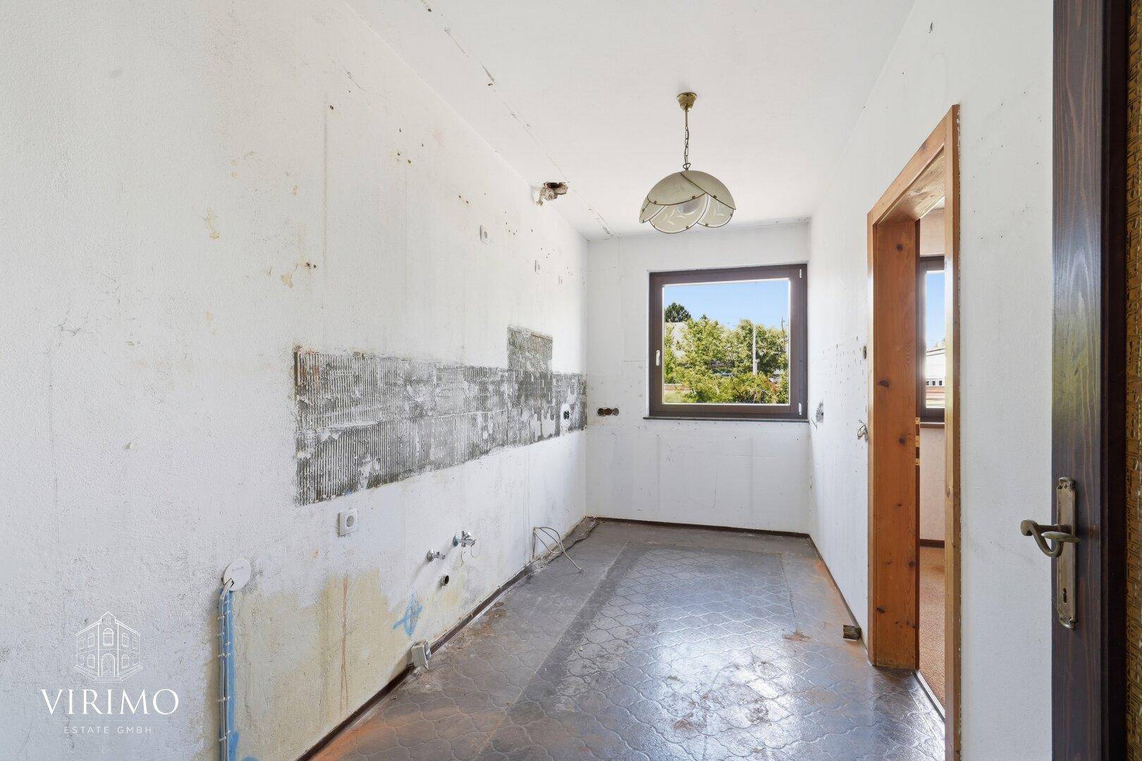 Renovierungsbedürftige Küche mit Fenster und vorbereiteten Anschlüssen.
