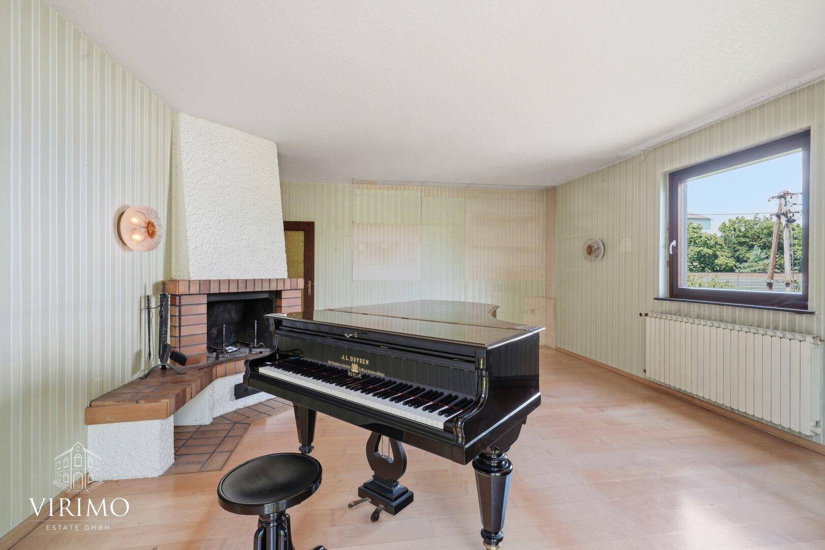 Geräumiges Wohnzimmer mit Kamin, Flügel und Blick ins Grüne.