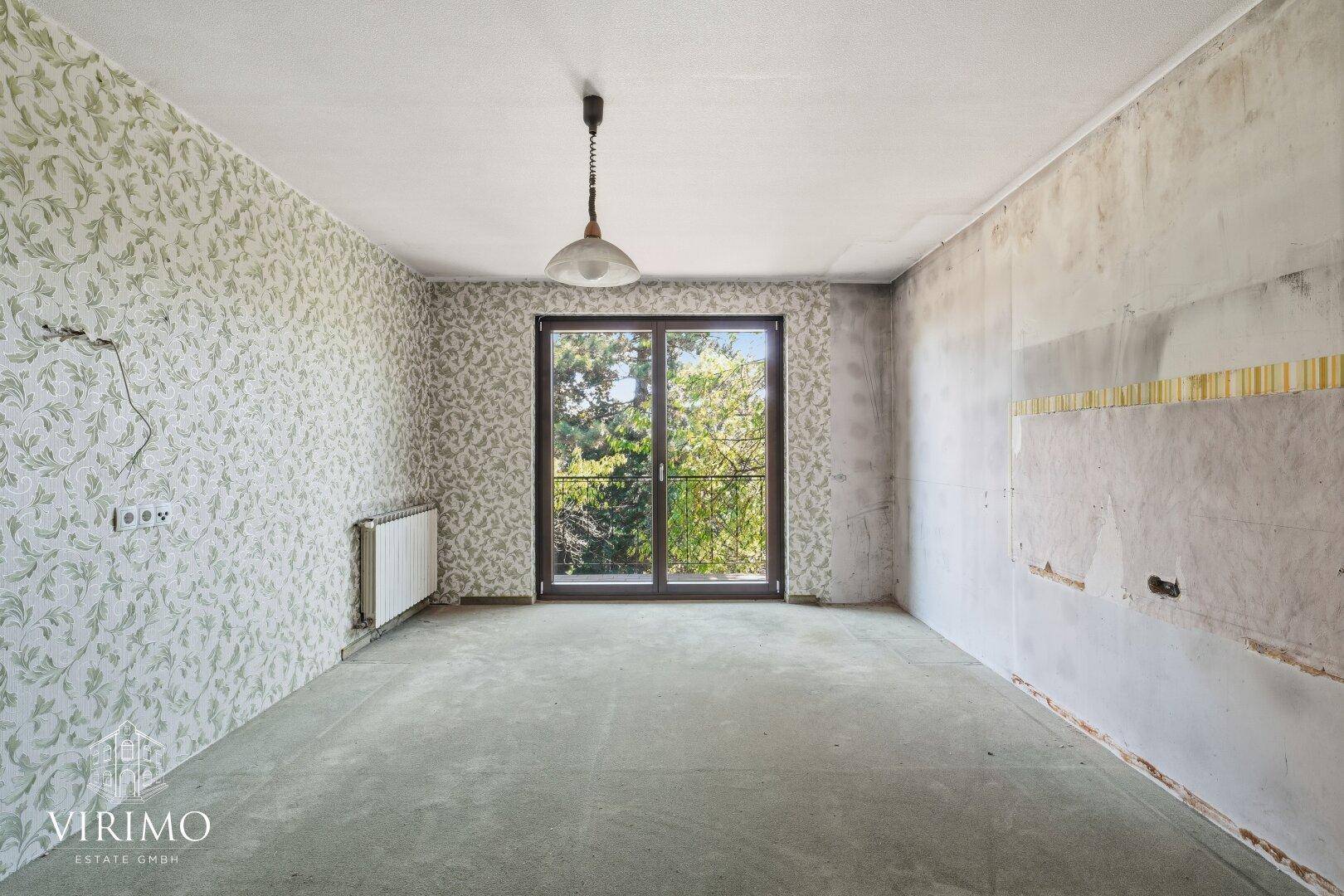 Renovierungsbedürftiger Raum mit Tapetenresten und Fensterblick ins Grüne.