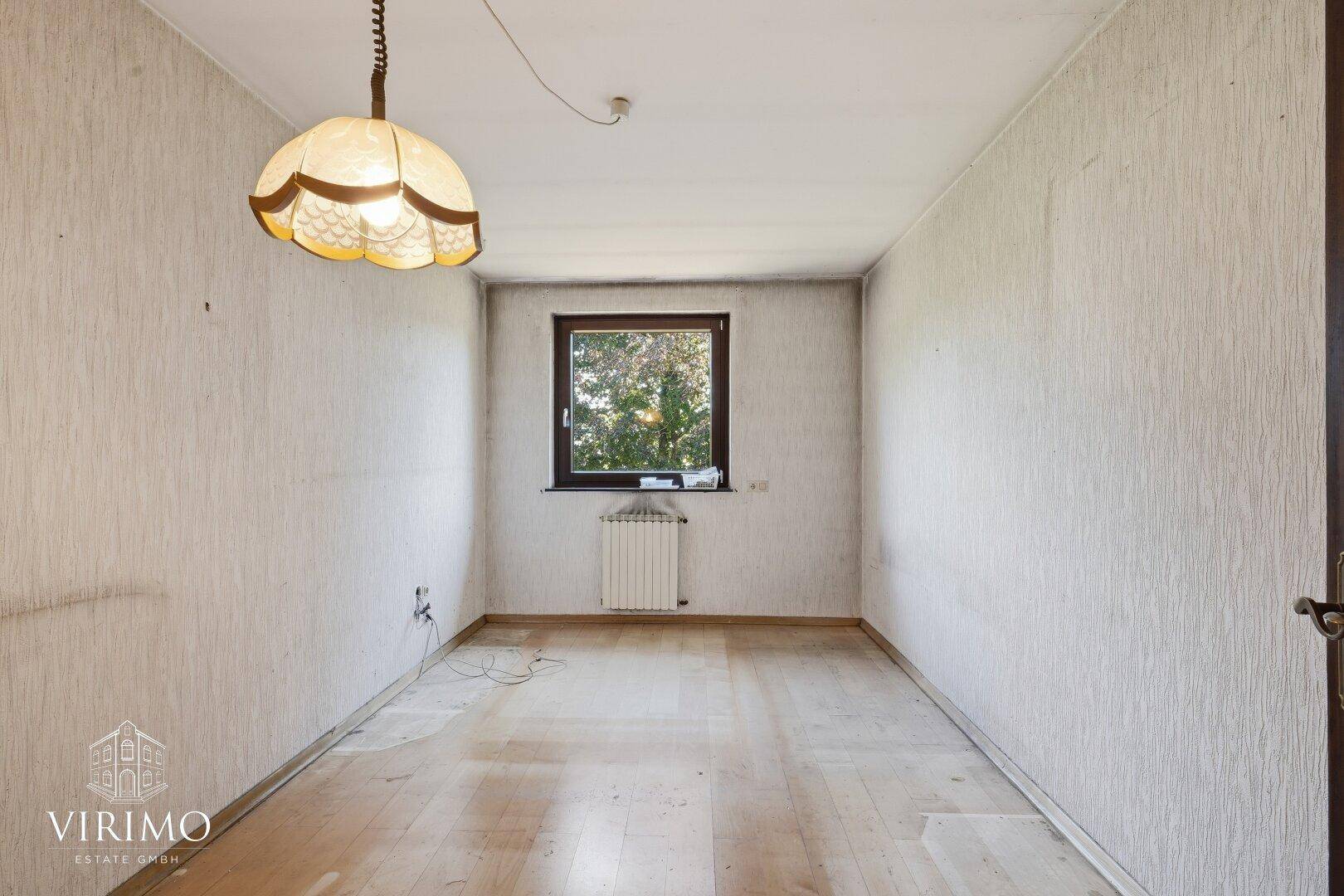 Kleiner Raum mit Fenster, Heizung und alten Tapeten, bereit zur Renovierung.