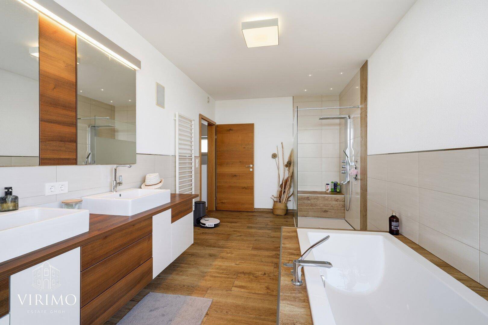 Helles Badezimmer mit Doppelwaschbecken, Dusche und beheiztem Handtuchhalter.