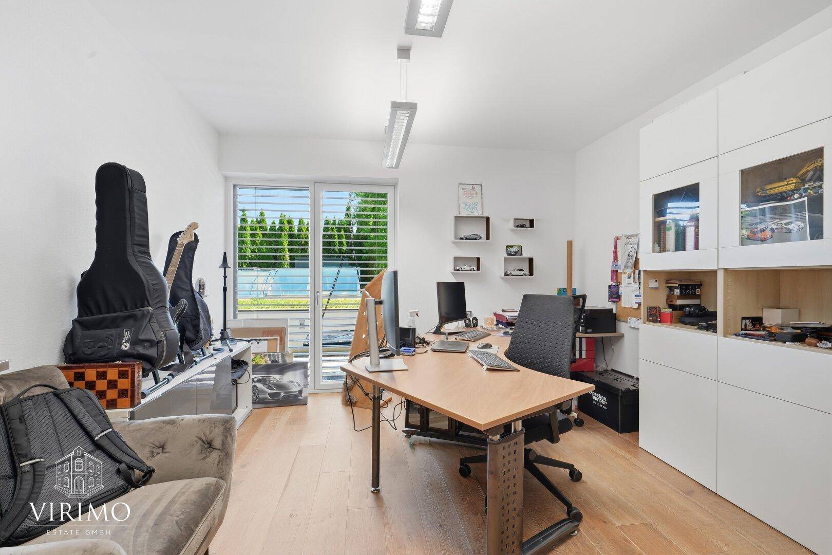 Geräumiges Büro mit Holzboden, Schreibtisch und Blick auf den Poolbereich.