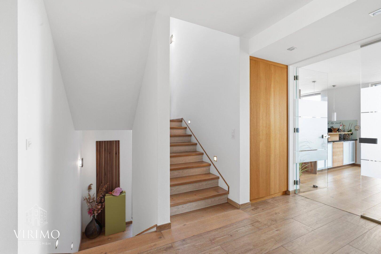 Heller Flur mit Holztreppe, Glaswand und Holzboden.