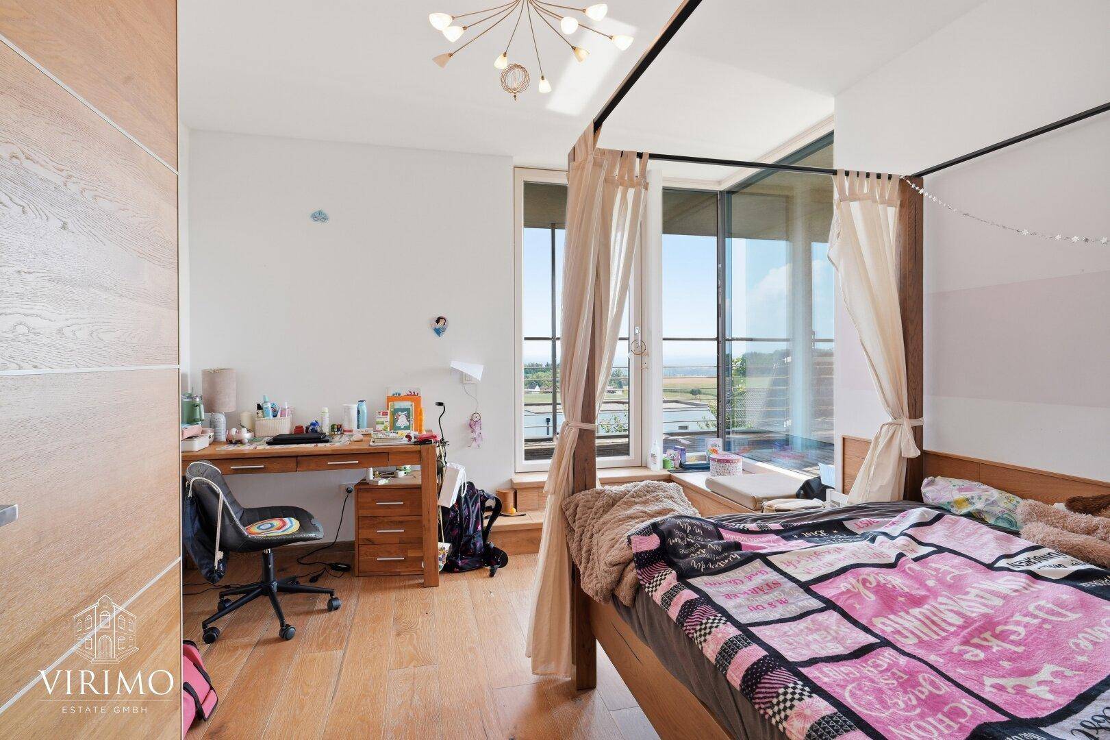 Helles Kinderzimmer mit Holzboden, Schreibtisch und großen Fenstern mit Ausblick.