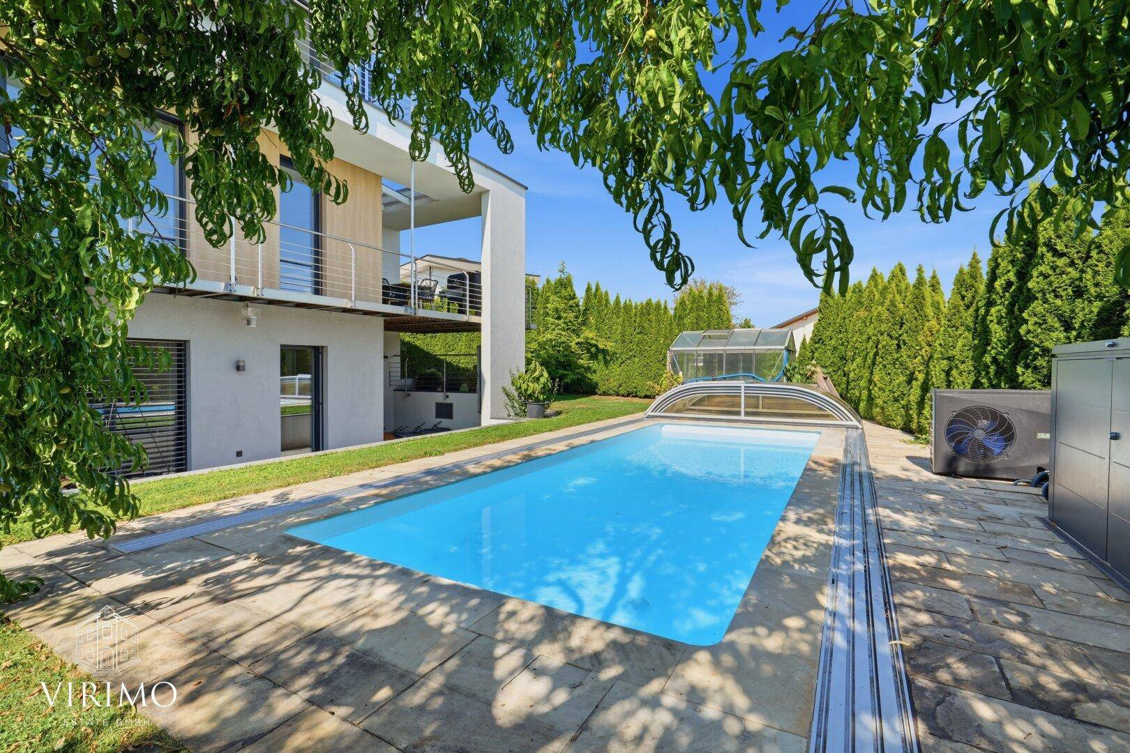 Gepflegter Außenbereich mit Pool und Poolabdeckung, umgeben von hohen Hecken und Bäumen.
