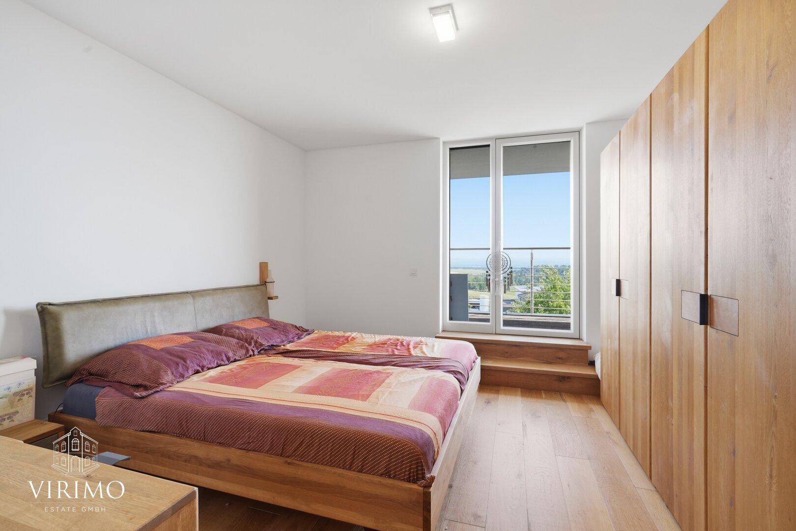Schlafzimmer mit Holzboden, Einbauschränken und Zugang zu einem französischen Balkon.